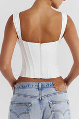 Back view of a woman wearing a white corset top with a zipper closure and light wash denim jeans.