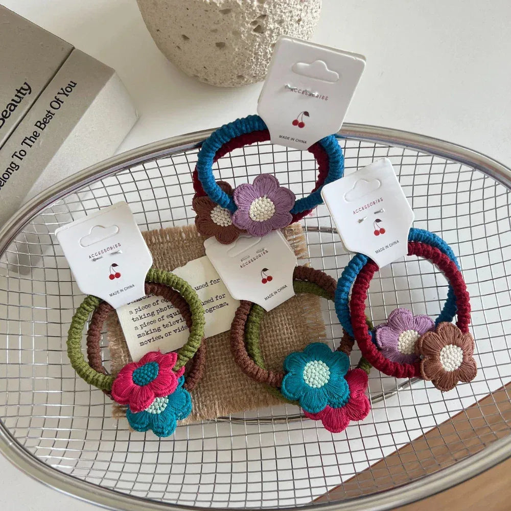 A collection of crocheted flower hair ties displayed in a wire basket.
