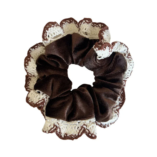 A brown velvet scrunchie with white and brown crocheted lace trim is shown against a white background.