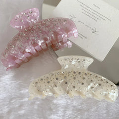 Two marbled claw clips, one pink and one cream, with rhinestones, placed on a fluffy white surface next to a card with text