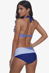 Woman wearing a blue and white polka dot halter neck bikini with high-waisted bottoms, back view.