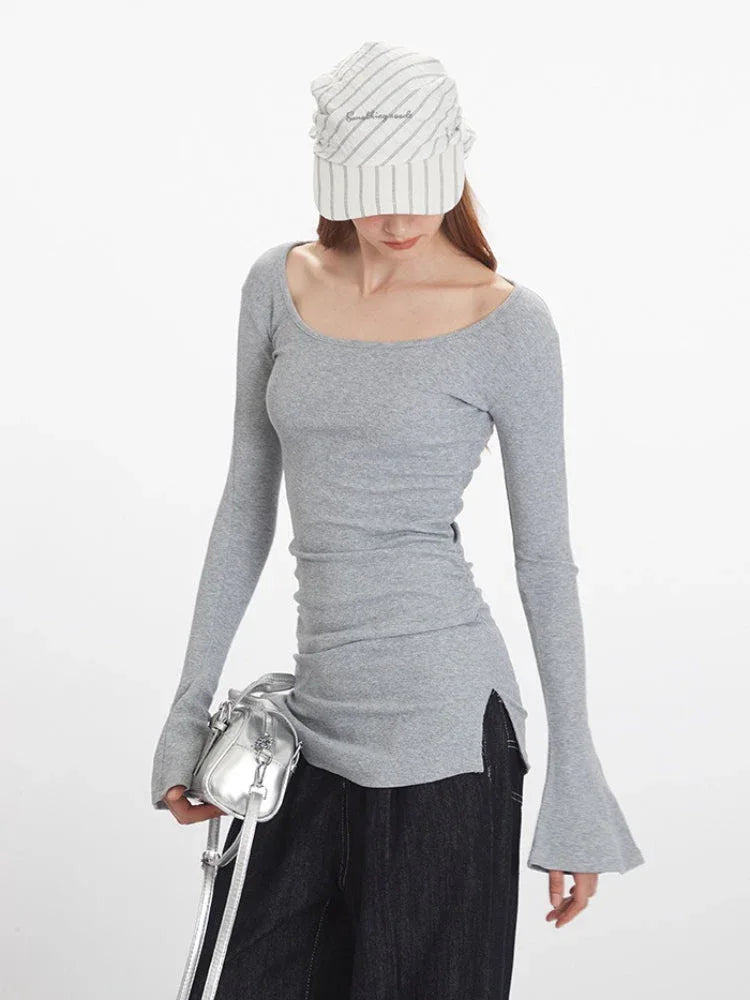 Close-up front view of a woman wearing a grey long-sleeve ribbed knit top with bell sleeves and dark wash wide-leg jeans, holding a silver handbag.