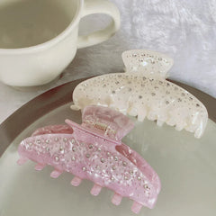 Two marbled claw clips, one pink and one cream, with rhinestones, placed on a plate next to a mug