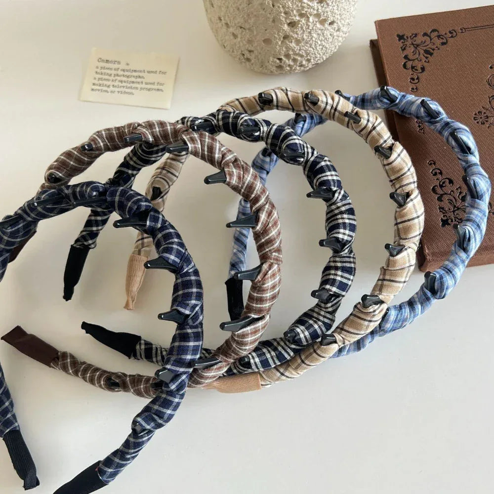 A pile of plaid fabric-wrapped headbands with black interlocking teeth on a white surface next to a book