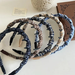A pile of plaid fabric-wrapped headbands with black interlocking teeth on a white surface next to a book