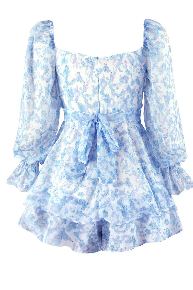 Close-up of the back of a white and blue floral print mini dress with long sleeves and a sweetheart neckline, showing a bow detail.