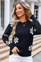 Woman wearing a black knit sweater with a white floral print and white pants.