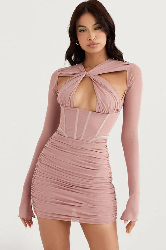Woman wearing a rose pink ruched bodycon dress with a cut-out halter neckline and long sleeves.