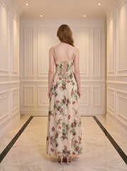 Back view of a woman in a cream-colored floral print maxi dress with spaghetti straps and a lace-up back detail, standing in a hallway.