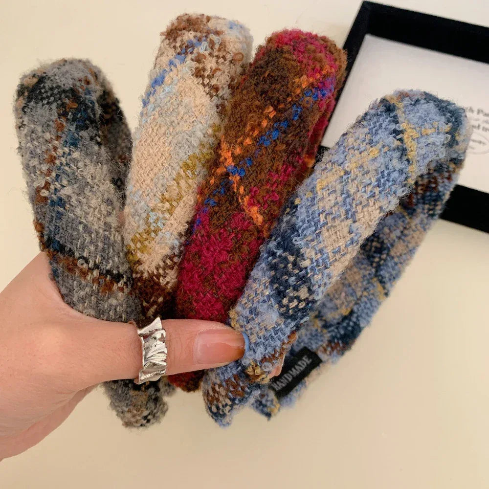 A hand holding four padded headbands with different plaid patterns.