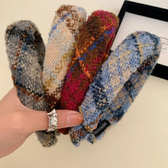 A hand holding four padded headbands with different plaid patterns.