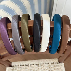 Collection of padded satin headbands in various colors (purple, grey, olive green, black, white, teal, brown) displayed on a wooden rack