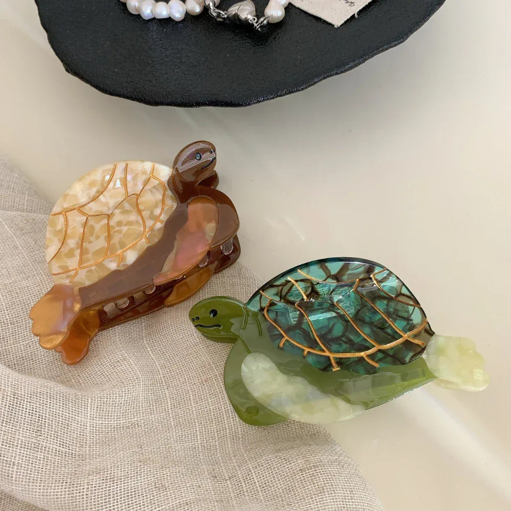 Two acetate turtle hair clips, one green and one brown/tan, on a neutral fabric background