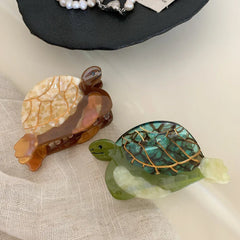 Two acetate turtle hair clips, one green and one brown/tan, on a neutral fabric background