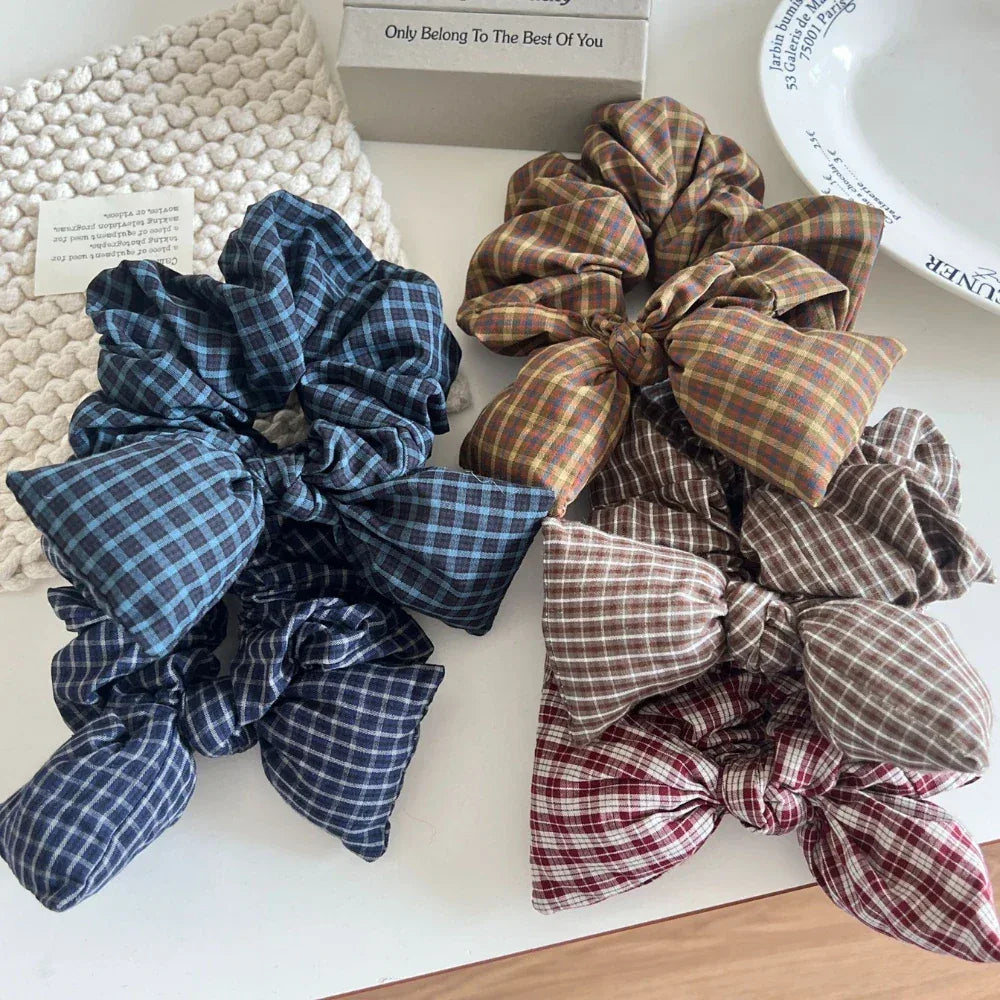 Assortment of plaid scrunchies with bow accents arranged on a white surface.
