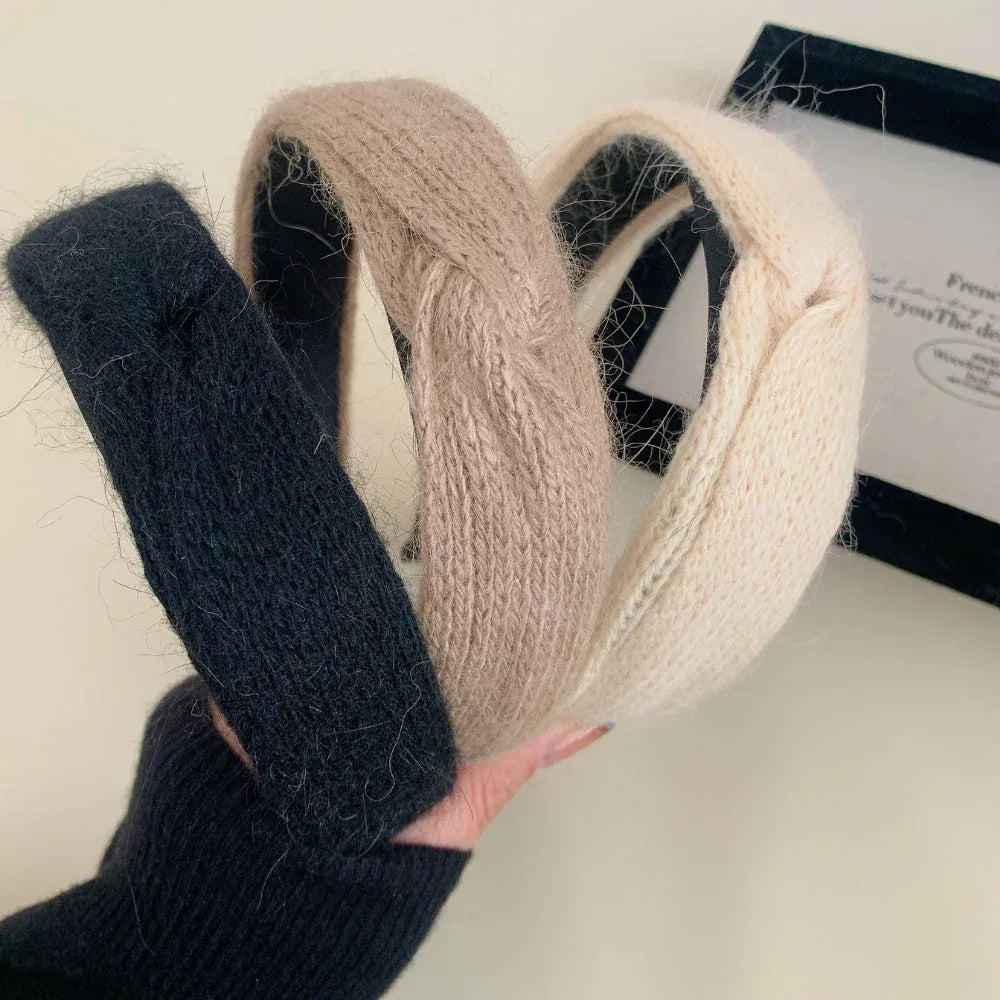 A hand holding three knit headbands in black, taupe, and cream