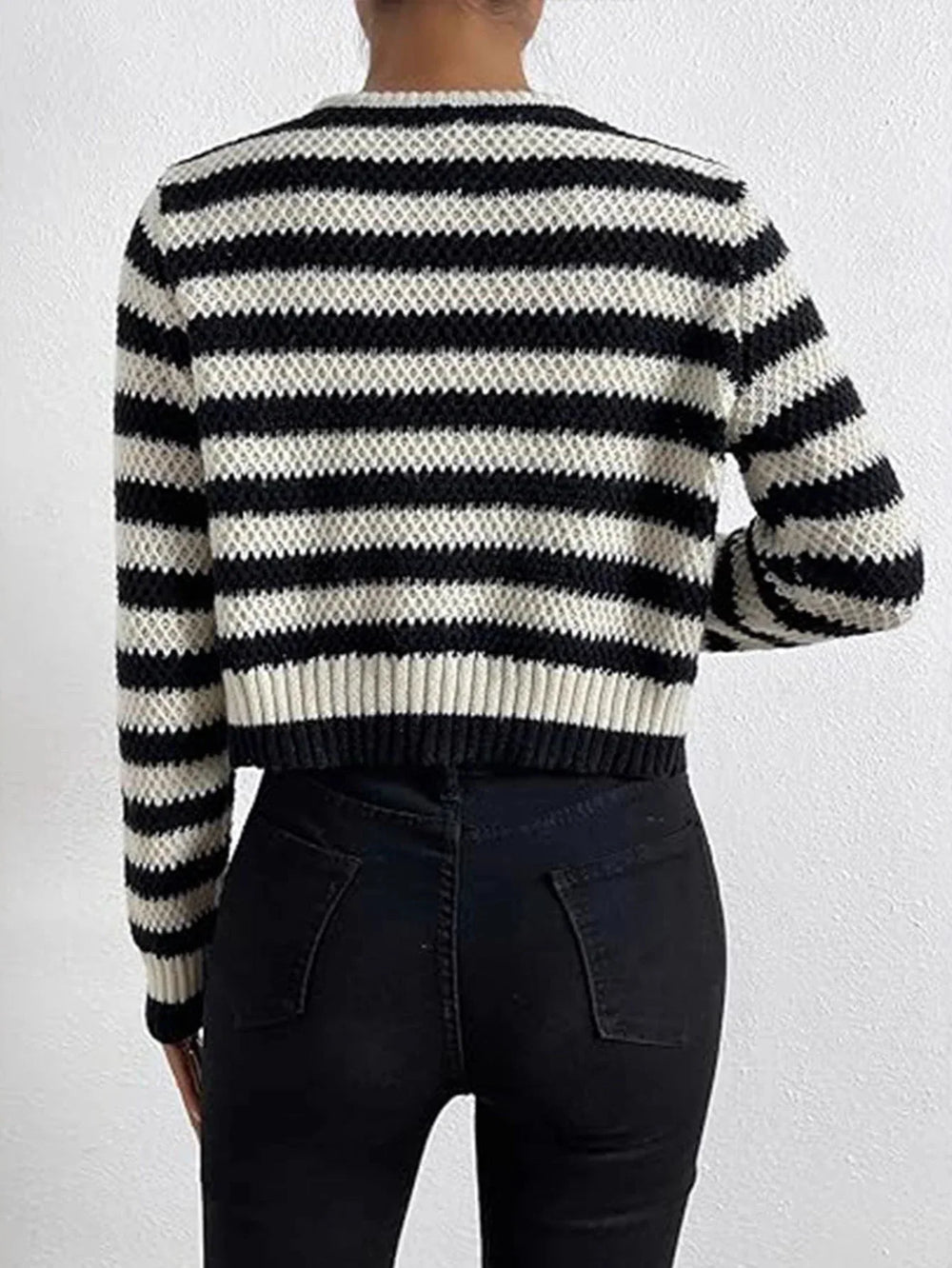 Back view of a woman wearing a black and white striped cropped knit cardigan and black jeans.