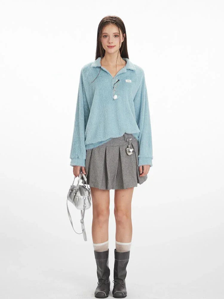 Model wearing a light blue fuzzy knit collared v-neck sweater with a grey pleated mini skirt, white and grey striped socks, and black boots.