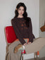 Young woman wearing a brown long-sleeved graphic t-shirt and beige pants, sitting on a red chair