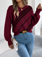 Woman holding a white handbag and wearing a burgundy knit sweater with black diagonal stripes, blue jeans, and a gold belt.
