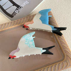 Two bird-shaped hair clips, one with blue wings and the other with blue-veined white wings, displayed on a tray.
