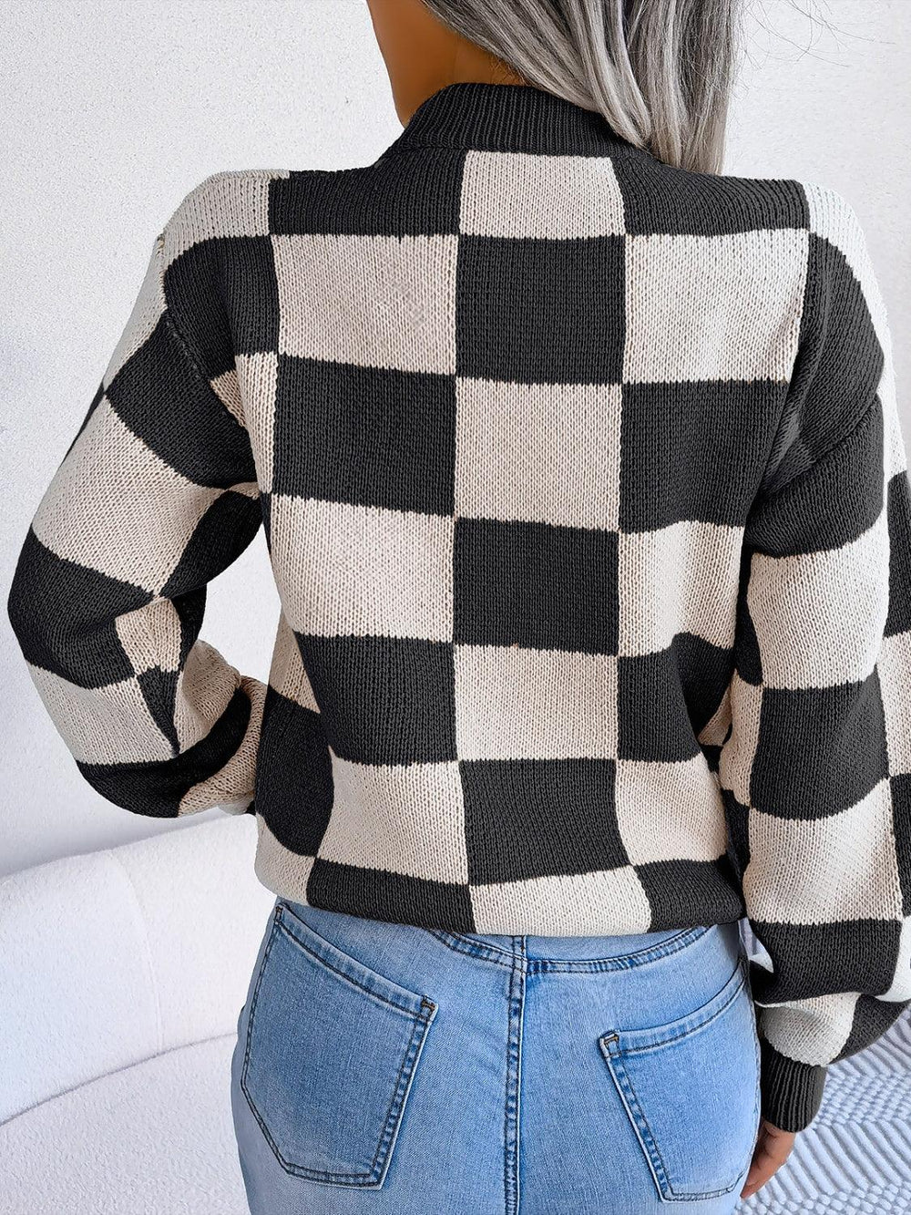 Woman wearing a black and white checkerboard knit sweater with light wash jeans, back view.