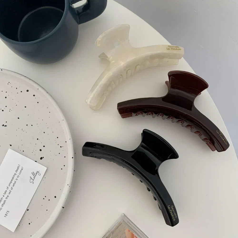 three hair claw clips in white, brown, and black on a white surface