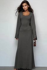 Woman wearing a long-sleeved, ribbed maxi dress with bell sleeves and a square neckline in a charcoal gray color, holding a small brown handbag.