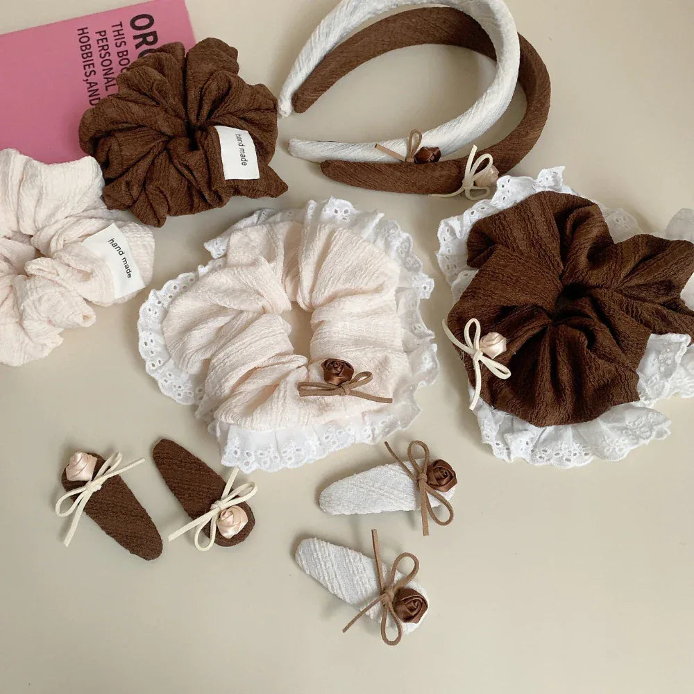 A collection of hair accessories including scrunchies, a headband, and hair clips in brown and cream colors, adorned with lace and floral details.