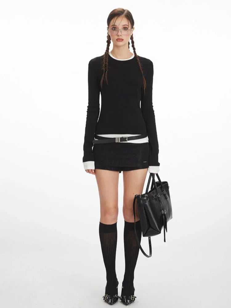 Woman wearing a black long-sleeved top with white trim, black shorts, black knee-high socks, and black heels, holding a black handbag.