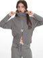 Woman zipping up a grey knit jacket, revealing a glimpse of white undergarment.