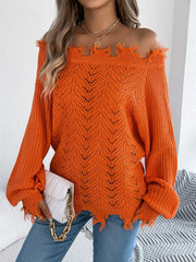 Close-up of a woman wearing an orange distressed off-the-shoulder knit sweater, holding a white clutch.