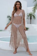 Woman wearing a beige open knit long tunic with fringe detailing and a side slit, standing by a pool.