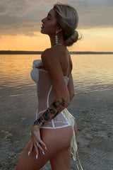 Side view of a woman wearing a white strapless boned corset with sheer panels and floral embellishments on a beach.