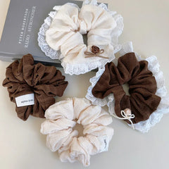 A group of four scrunchies, two in cream and two in brown, some with lace trim and floral accents, arranged on a white surface.