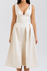 Woman wearing an ivory midi dress with a deep V-neck and pleated skirt.
