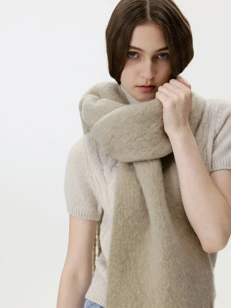 Woman wearing a beige knit sweater and a beige fuzzy scarf wrapped around her neck.