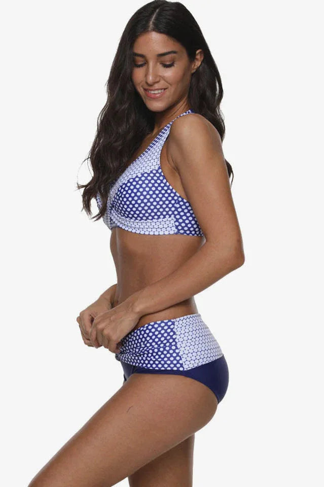 Woman wearing a blue and white polka dot halter neck bikini with high-waisted bottoms, side view.