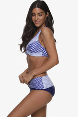 Woman wearing a blue and white polka dot halter neck bikini with high-waisted bottoms, side view.
