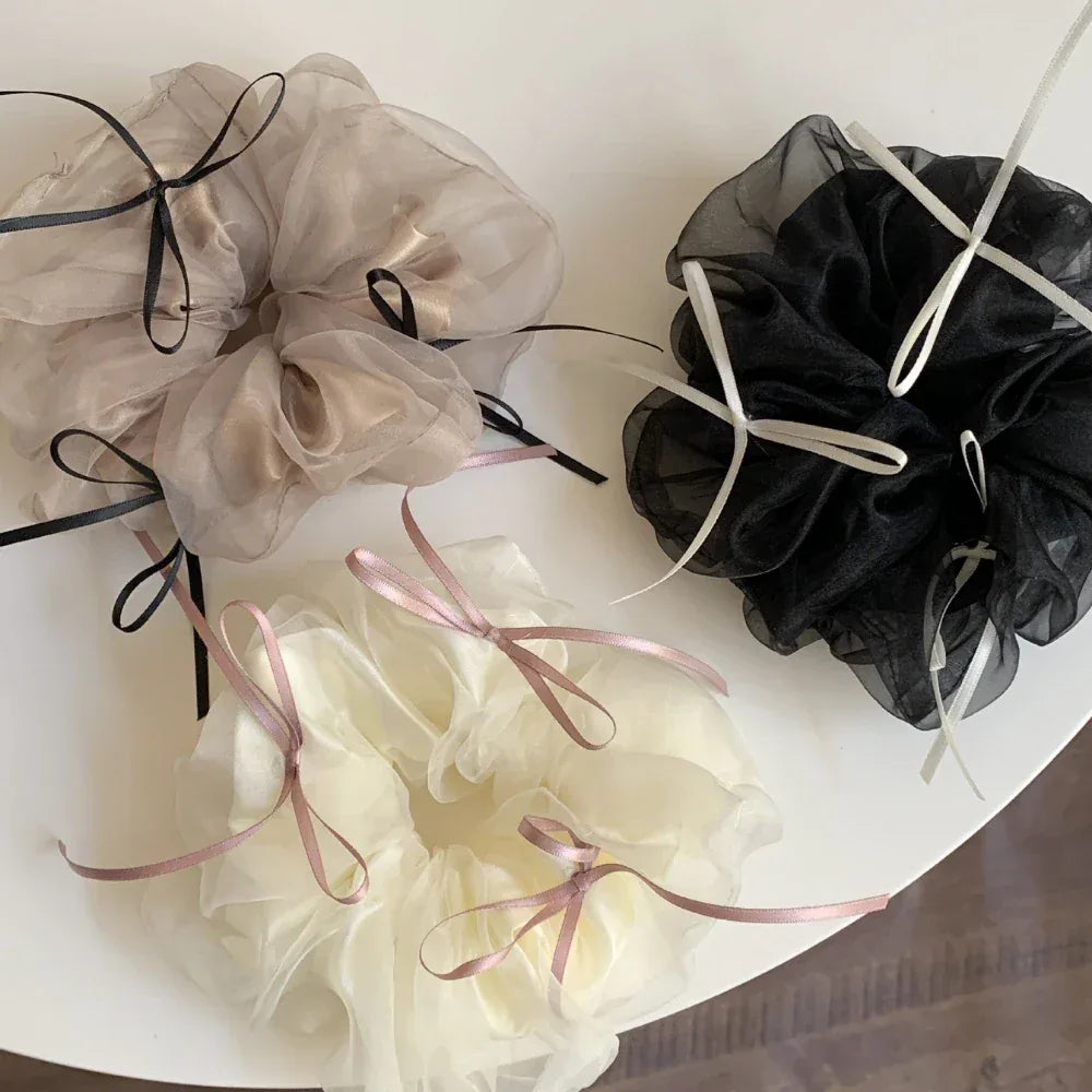 A top-down arrangement of three voluminous scrunchies in ivory, taupe, and black, highlighted by their ribbon embellishments.