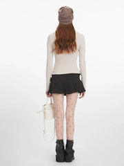 Back view of a woman wearing a cream long-sleeve top with fur trim, a black pleated mini skirt, decorative tights, and black boots, holding a white bucket bag.