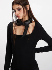 Close-up of a woman's face and upper body, wearing a black long-sleeve top with a scarf detail.