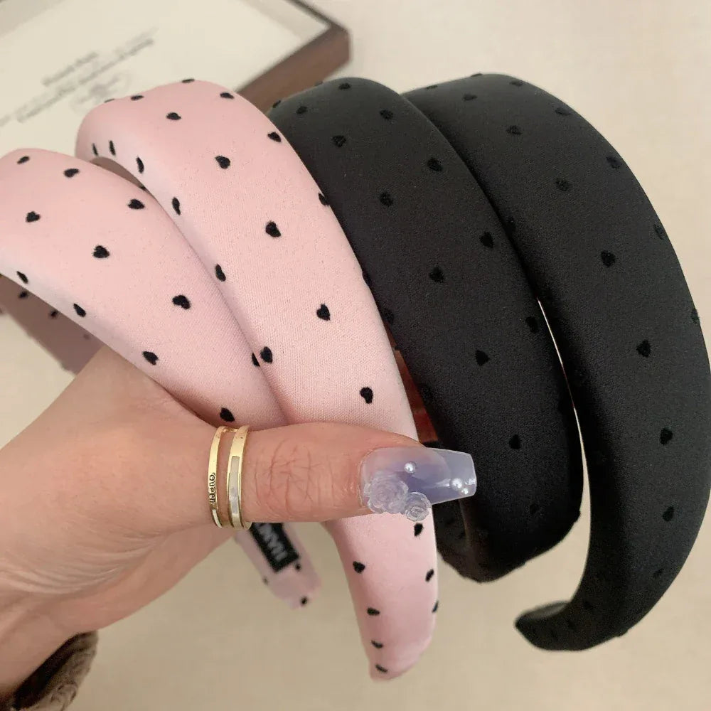 A hand holding three puffy headbands in pink and black with a heart print.