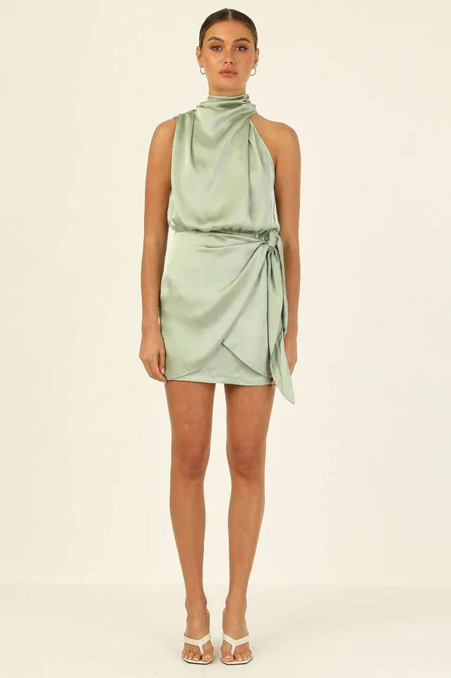 full body shot of a woman wearing a sage green satin halter neck mini dress