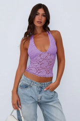 Woman wearing a purple lace halter top with blue jeans, side view