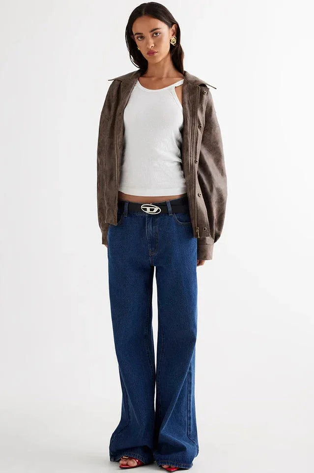 Front view of a model in a brown faux leather jacket, white tank top, and blue wide-leg jeans