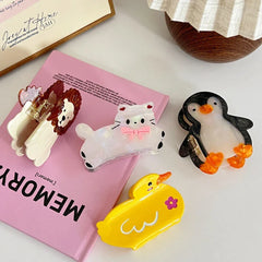 collection of animal hair claw clips including a cat, lion, penguin, and duck arranged on a pink book