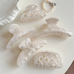 A collection of cream-colored marbled acetate hair clips and a pearl bracelet arranged on a light surface.