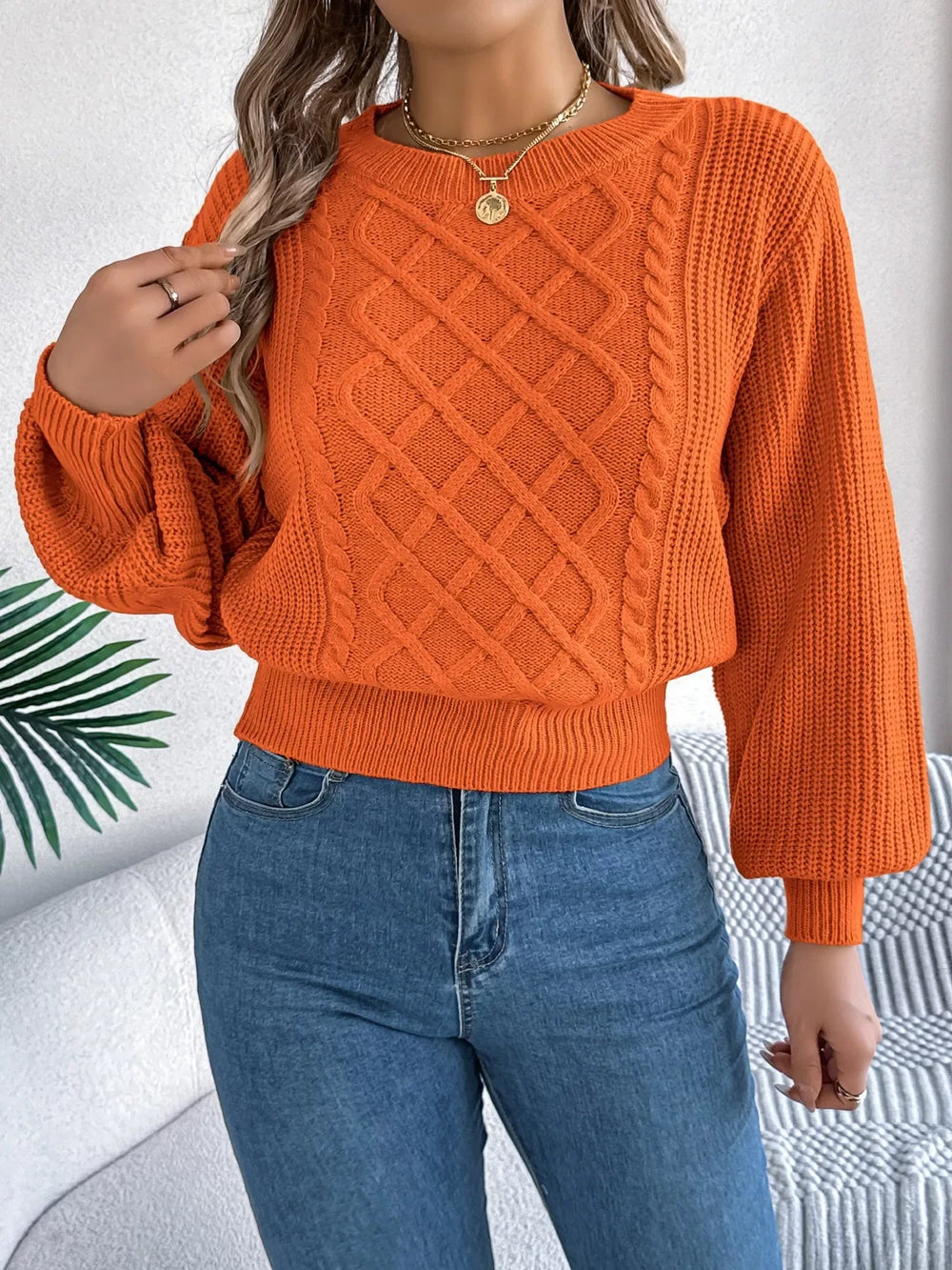 Close-up of a woman wearing an orange cable knit sweater with blue jeans and a necklace