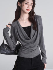 Model holding a black handbag while wearing a grey long-sleeved top with a draped neckline.
